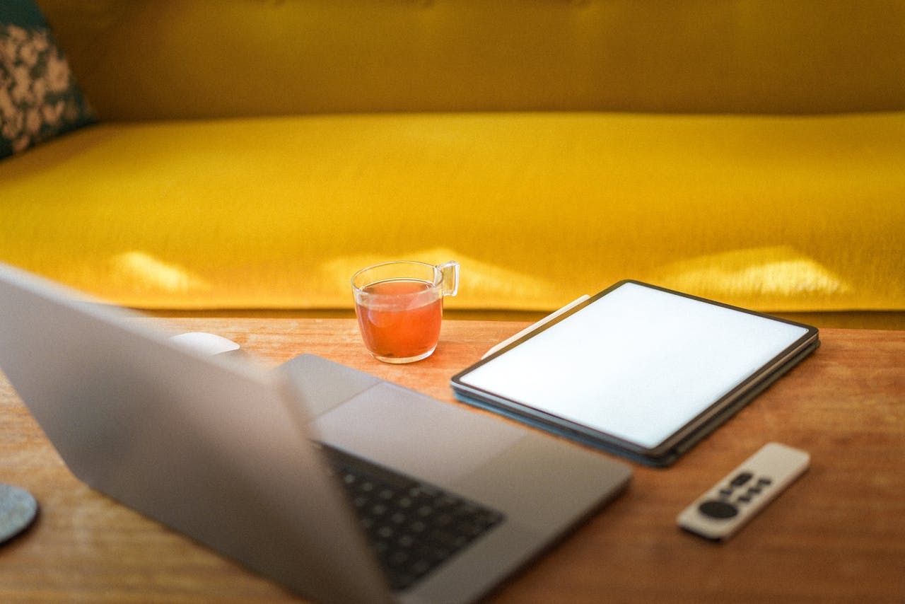Cozy workspace with a laptop, tablet, and tea on a wooden table in a modern living room.